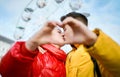 Young romantic couple on date, embracing and kissing through a heart gesture made with their fingers, spending time