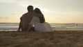 Young romantic couple is enjoying beautiful sunset sitting on the beach and hugging. A woman and a man sits together in Royalty Free Stock Photo