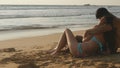 Young romantic couple is enjoying beautiful view sitting on the beach and hugging. A woman and a man sits together in Royalty Free Stock Photo