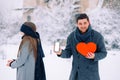 Young romantic couple, surprise outdoor, winter time. Man holding red heart and mobile phone with blank empty screen Royalty Free Stock Photo