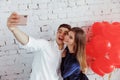 Young romantic loving beautiful couple guy with a girl with red heart shaped air balloons take a selfie on the phone on an Royalty Free Stock Photo