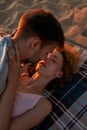 Young romatic couple in love kissing and cuddling while lying together on the beach at sunset