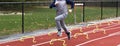 Young runner running over yellow six inch hurdles during track practice