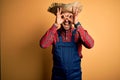 Young rural farmer man wearing bib overall and countryside hat over yellow background doing ok gesture like binoculars sticking Royalty Free Stock Photo