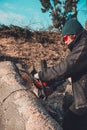 Young rural girl cut a tree chainsaw in gloves, cook firewood for winter