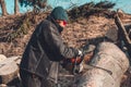 Young rural girl cut a tree chainsaw in gloves, cook firewood for winter