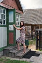 Young rustic teacher woman in retro dress with old-fashioned suitcase opens the door of a rural school holding the door handle Royalty Free Stock Photo