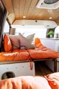 Young 30s caucasian woman with dark hair making the bed in a self converted minivan campervan for van life with lovely light