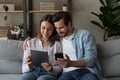 Couple sit on sofa with modern diverse gadgets