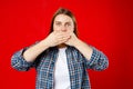 Young 30s woman covering closed mouth with hands open eyes. Speak no evil concept isolated red background. Human emotion