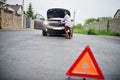 Young sad african woman stand with emergency triangle against car with popped hood. Transportation, vehicles problems and Royalty Free Stock Photo