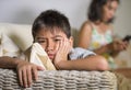 Young sad and bored Asian child at home couch feeling frustrated and unattended while mother networking on mobile phone as Royalty Free Stock Photo