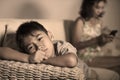 Young sad and bored Asian child at home couch feeling frustrated and unattended while mother networking on mobile phone as Royalty Free Stock Photo