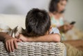 Young sad and bored Asian child at home couch feeling frustrated and unattended while mother networking on mobile phone as Royalty Free Stock Photo