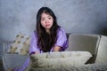 Young sad and depressed Asian Chinese woman crying alone desperate sitting at home sofa ouch worried in pain and stress suffering