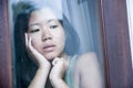 Young sad and depressed Asian Chinese woman looking thoughtful through window glass suffering pain and depression in sadness conce Royalty Free Stock Photo