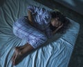 Young sad and depressed hispanic woman with curly hair sleepless in bed suffering excruciating period pain holding her belly in Royalty Free Stock Photo