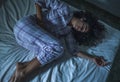 Young sad and depressed middle eastern woman with curly hair sleepless in bed suffering excruciating period pain holding her belly Royalty Free Stock Photo