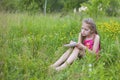 A young sad girl is sitting on a green grass and writing something in a paper notebook Royalty Free Stock Photo