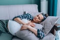 Young sad lonely pregnant woman lying on sofa at home having depressed mood