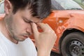Young sad man had car accident. Damaged car in background