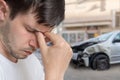 Young sad man had car accident. Damaged car in background.