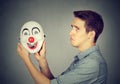 Young sad man with happy clown mask. Human emotions