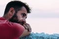 Young sad man by the sea looking at water