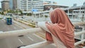A young, sad Muslim girl stands on a bridge over road traffic in downtown Jakarta. Indonesia.