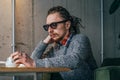 Young sad thoughtful man in glasses and dreadlocks sitting alone in cafe Royalty Free Stock Photo