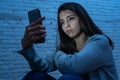 Young sad woman alone looking at smart phone in fear suffering Internet harassment and cyberbullying