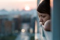 Young sad woman looking outside through balcony