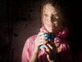 Young sad woman portrait behind the window in the rain with rain drops on it. girl holding a cup of hot drink Royalty Free Stock Photo