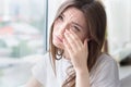 Young sad woman sits alone front of the window. Crying girl. Allergy, illness, depression, stress