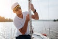 Young sailor in sunglasses and cap holds and moves ropes with both hands. He is calm and concentrated. Young man is Royalty Free Stock Photo