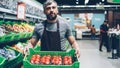 young salesman in apron carrying box of tomatoes in supermarket in fruit and vegetables department. Salesperson, food Royalty Free Stock Photo