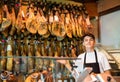 Young salesman in black apron offering dry-cured jamon in butcher shop