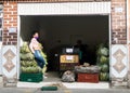 Young saleswoman selling plantains, bananas in her garage. Wearing a mask to avoid the spread of coronavirus; sitting on the fruit