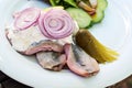 Young salted fish called soused or matjes herring with sour cream, gherkin and red onions, served with salad on a white plate,