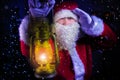 Young santa clause, carrying lantern looks through blizard of snow with christmas tree and street lamp in background Royalty Free Stock Photo