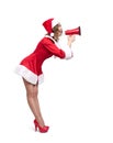 Young Santa woman in a red suit with heels, screaming by megaphone, side view,  on a white background Royalty Free Stock Photo