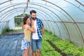 Young satisfied family couple standing in the greenhouse and smiling looking at the vegetables they planted as small business and