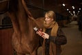 Young satisfied woman grooming horse with electric shaver in ranch stable Royalty Free Stock Photo