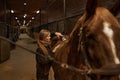 Young satisfied woman grooming horse with electric shaver in ranch stable Royalty Free Stock Photo