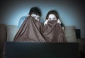 Young scared couple is watching horror on TV. Pair is covering with blanket