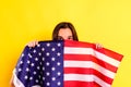 Young scared latin woman covers herself with an american flag in fear of deportations,  on yellow background Royalty Free Stock Photo