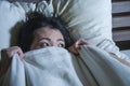 Young scared and stressed Asian Chinese woman lying in bed suffering nightmare in fear and panic grasping blanket covering her hor