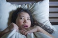 Young scared and stressed Asian Chinese woman lying in bed suffering nightmare in fear and panic grasping blanket covering her hor Royalty Free Stock Photo