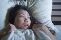 Young scared and stressed Asian Chinese woman lying in bed suffering nightmare in fear and panic grasping blanket covering her hor Royalty Free Stock Photo