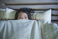 Young scared and stressed Asian Chinese woman lying in bed suffering nightmare in fear and panic grasping blanket covering her hor Royalty Free Stock Photo